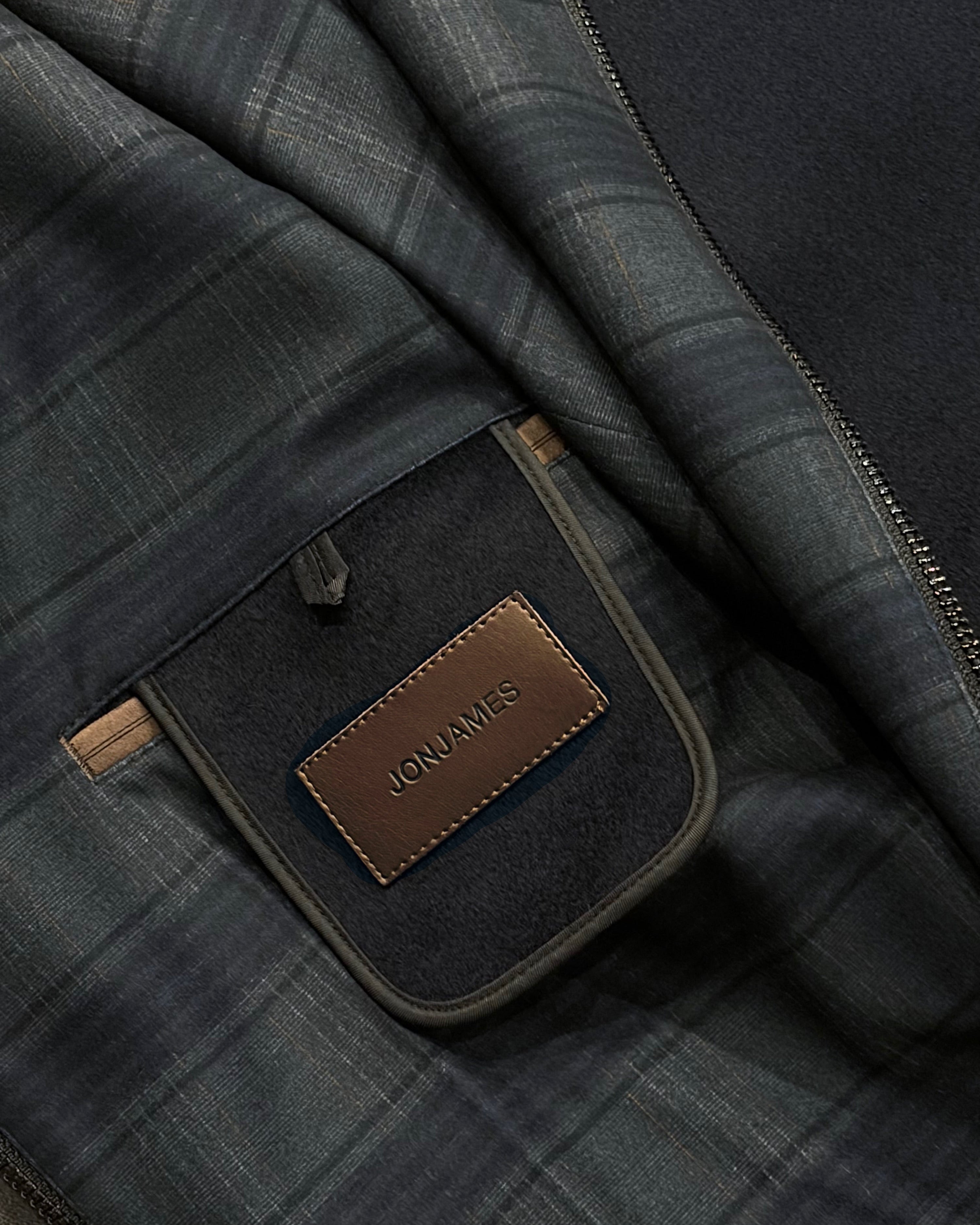 Close-up of a dark plaid fabric with a leather patch and 'JONJAMES' branding.