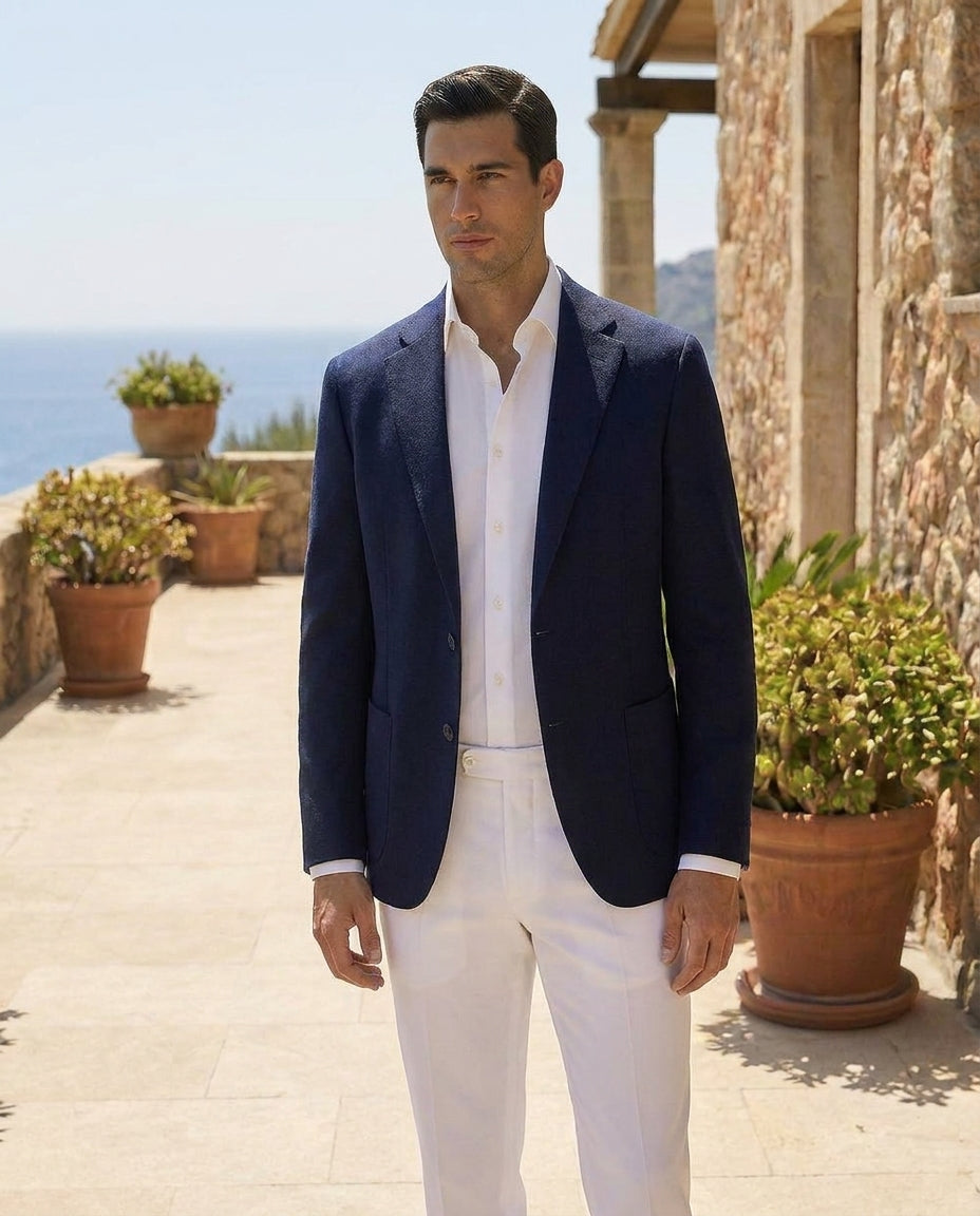 Man in navy blazer and white pants standing outdoors with ocean view