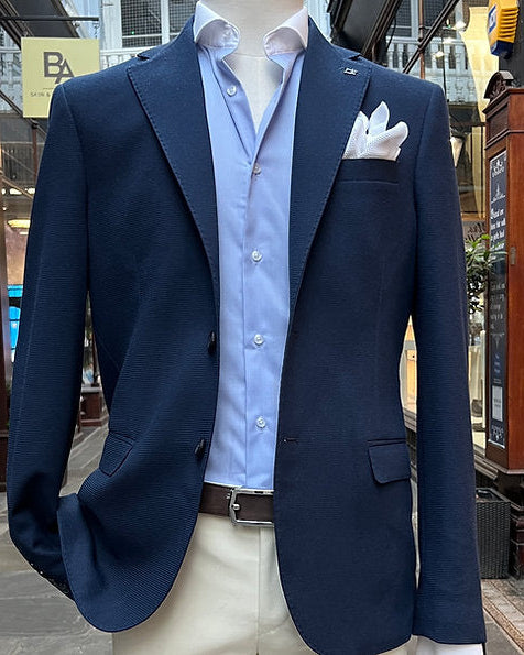 Navy blazer over a light blue shirt with white pants on a mannequin in an urban setting.