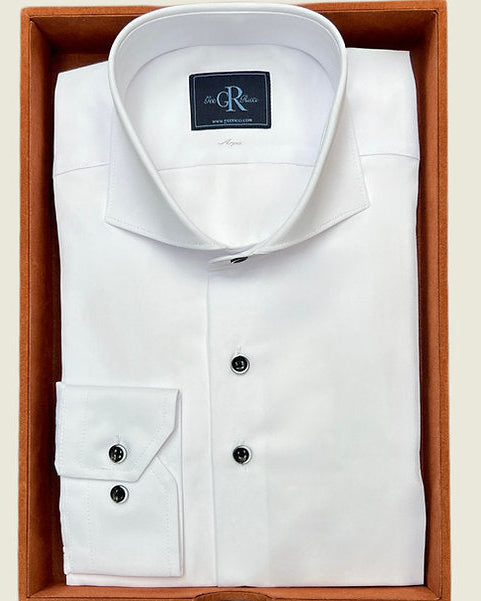 A white dress shirt with a cutaway collar, dark navy buttons with white contrast trim, and a double-button cuff, displayed in a wooden box.