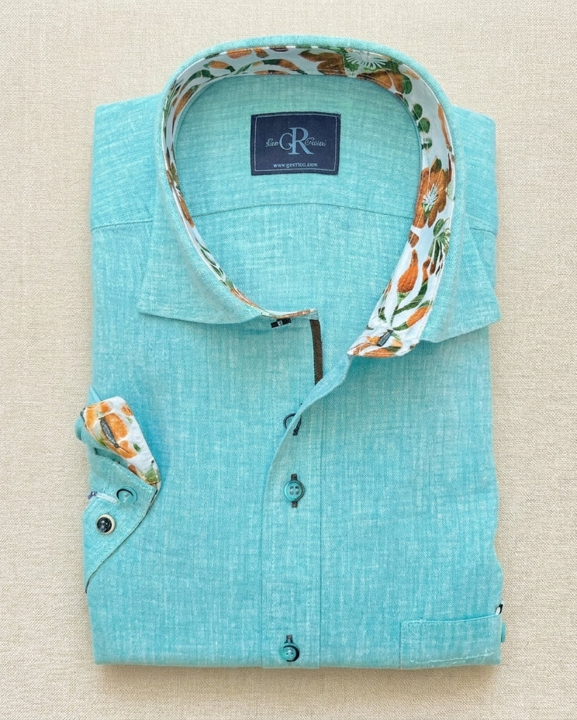 Folded turquoise shirt with floral trim on a beige background