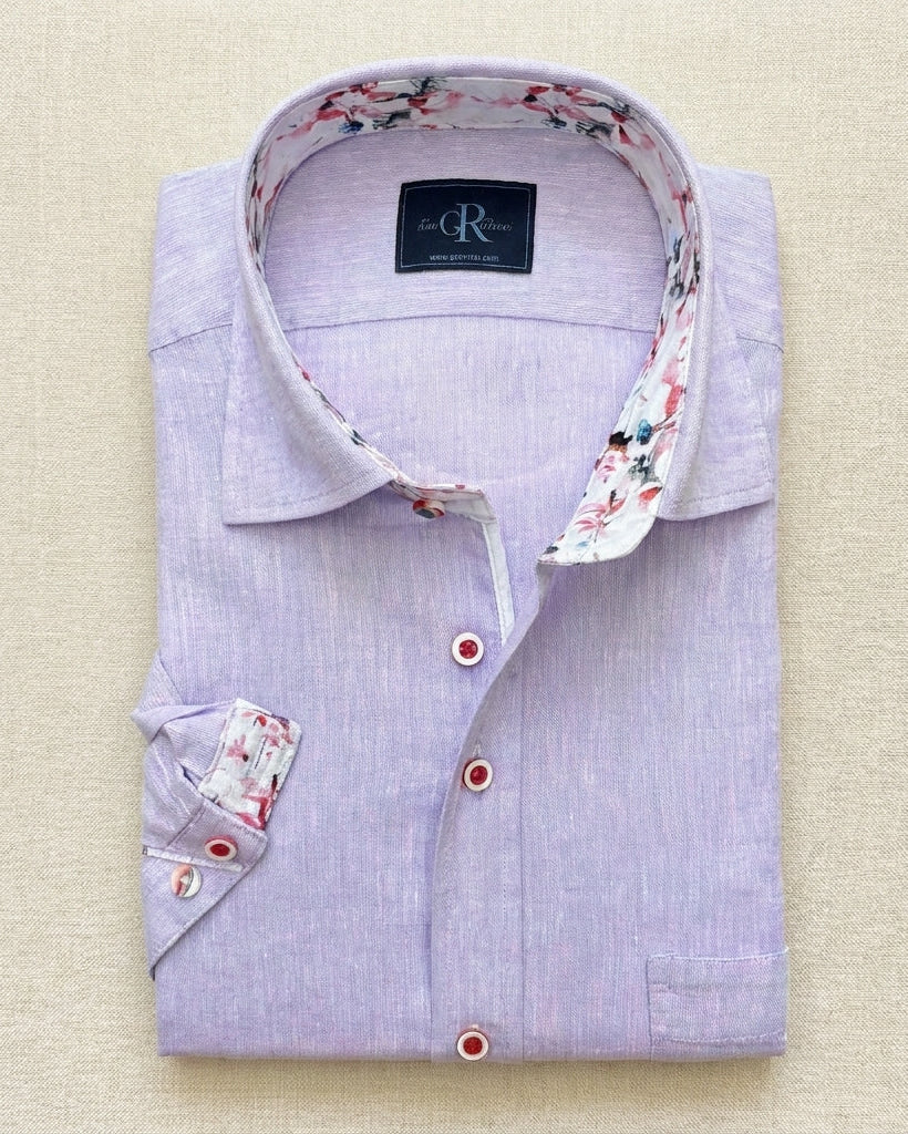 Folded light purple dress shirt with floral trim on a beige background
