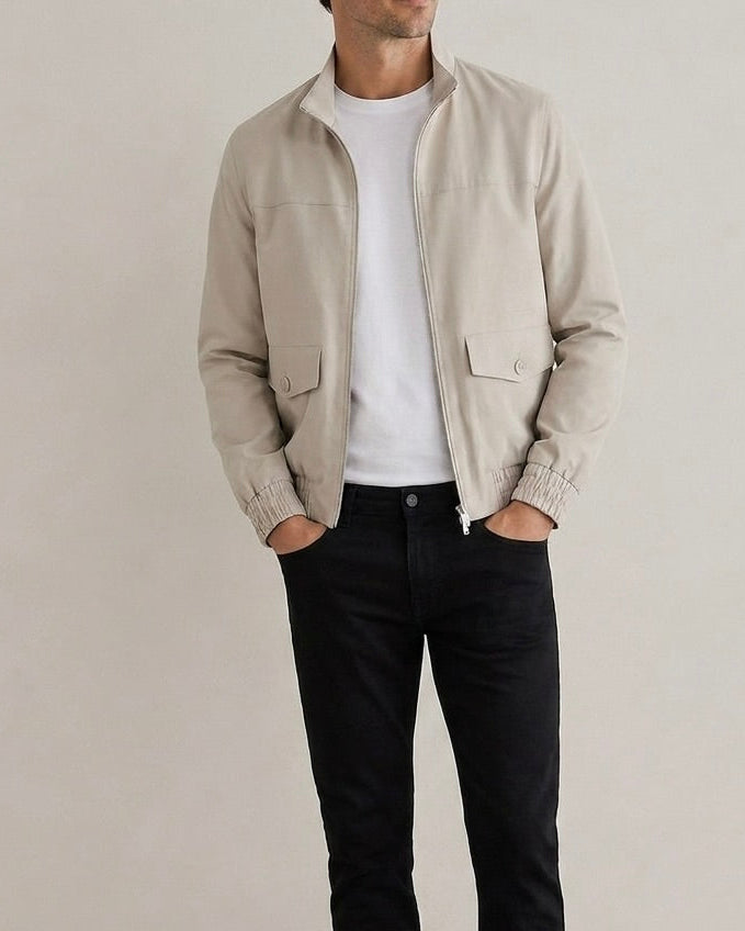 Person wearing a beige jacket over a white shirt and black pants on a plain background