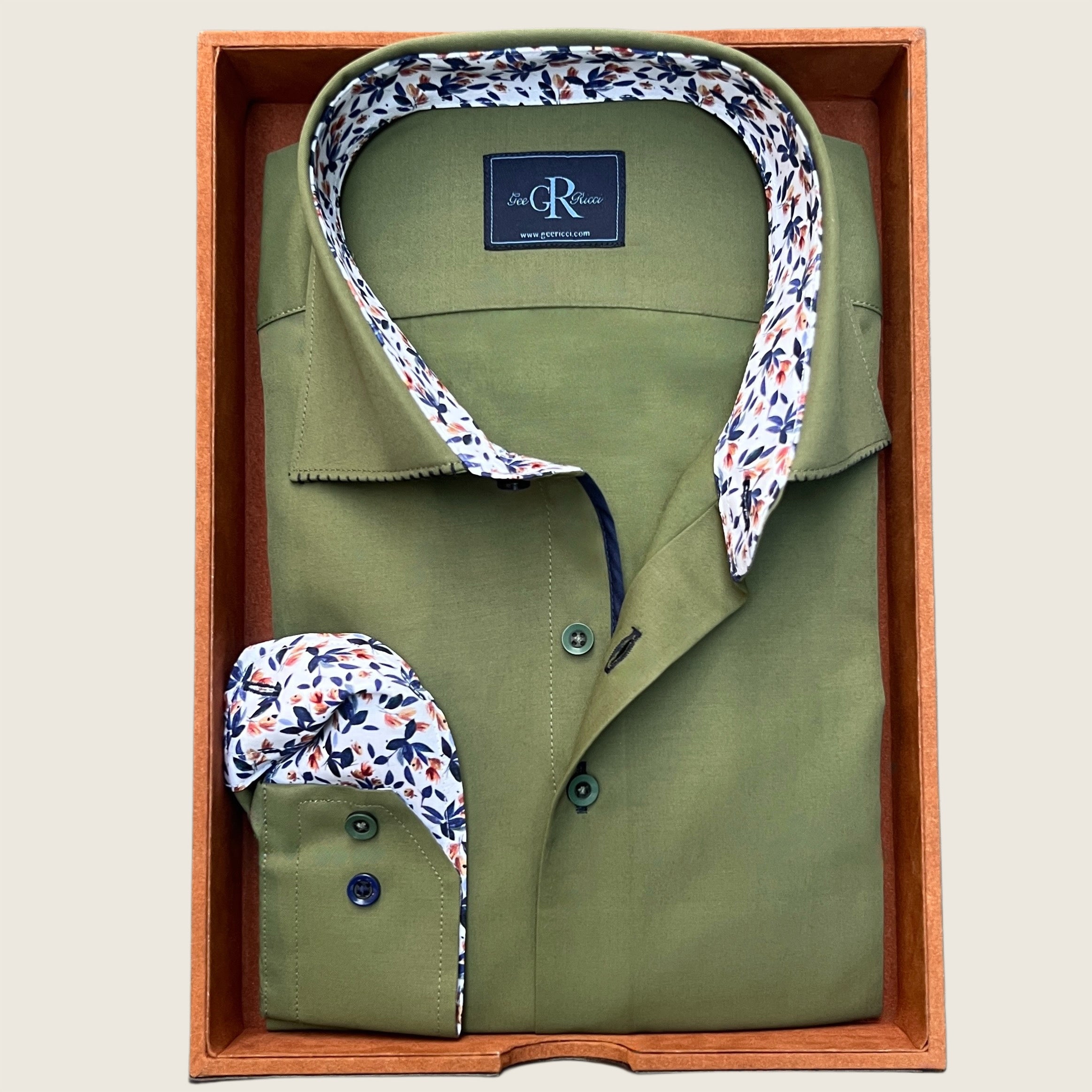 An olive green long-sleeve shirt with a floral print inner collar and cuffs, displayed in a wooden box.