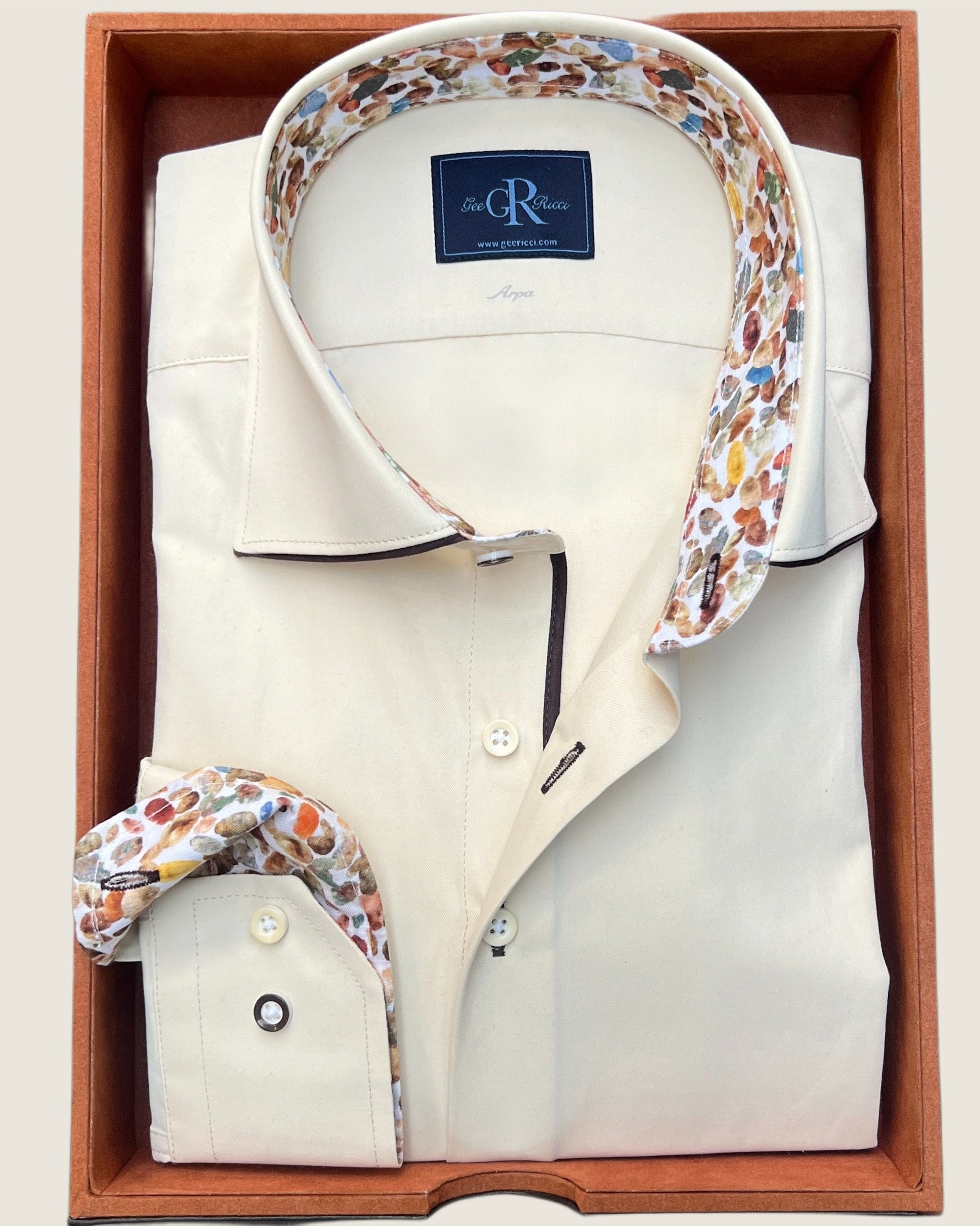 A champagne-colored Riviera shirt with a hidden button-down collar and contrast trim on the cuffs and collar, displayed in a wooden box.
