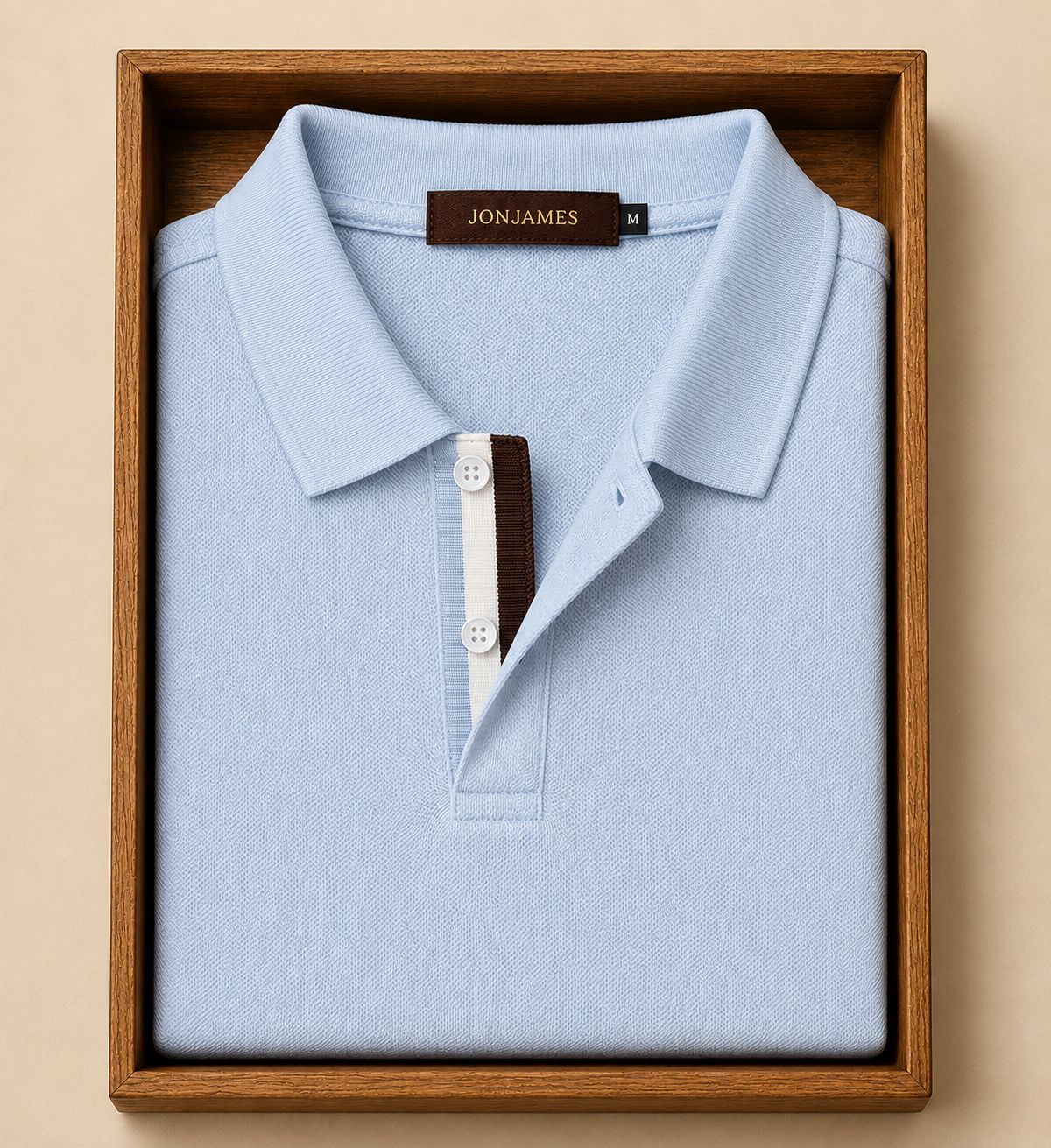 Light blue polo shirt with 'Jon James' label in a wooden box on a beige background