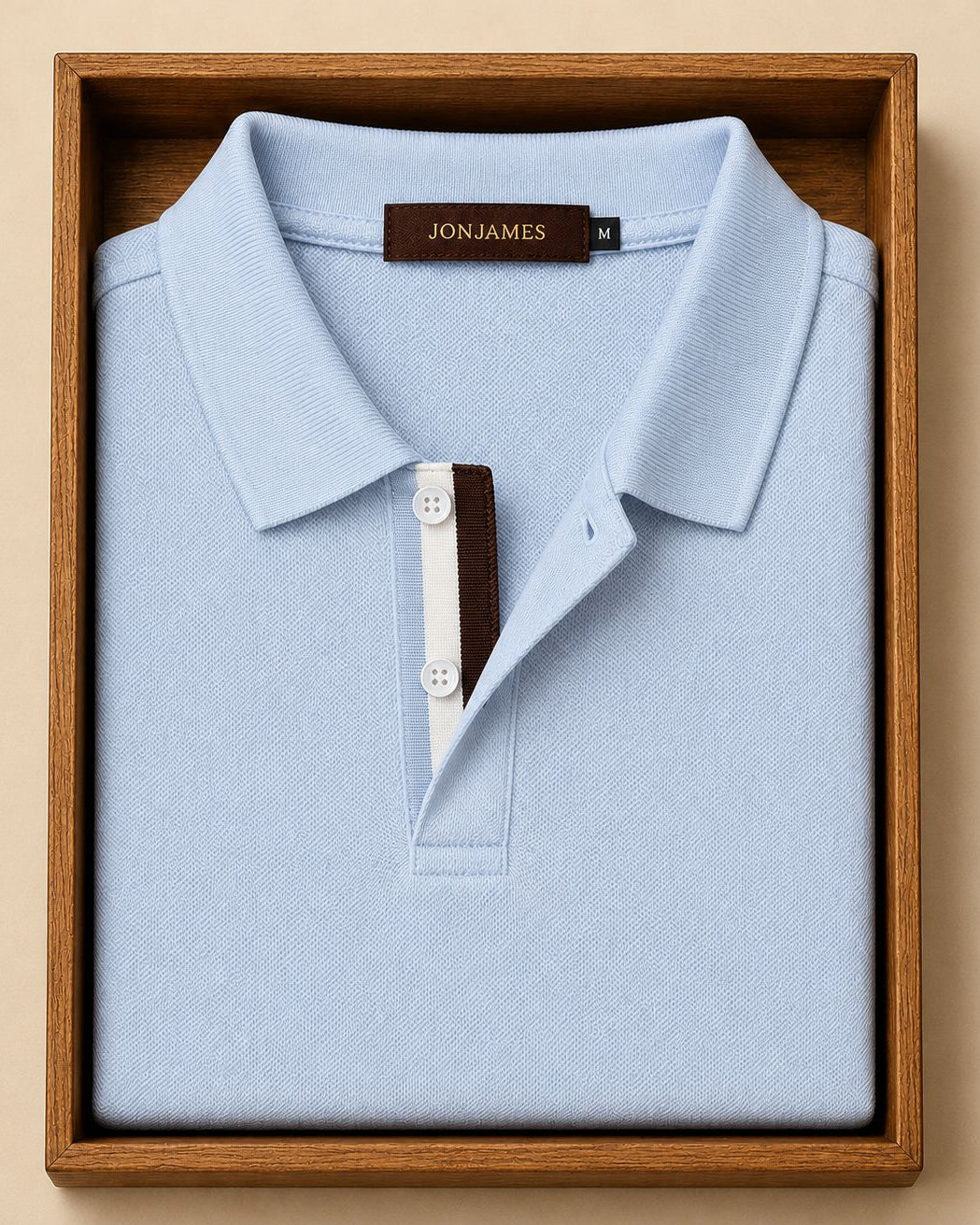 Light blue polo shirt with 'Jon James' label in a wooden box on a beige background