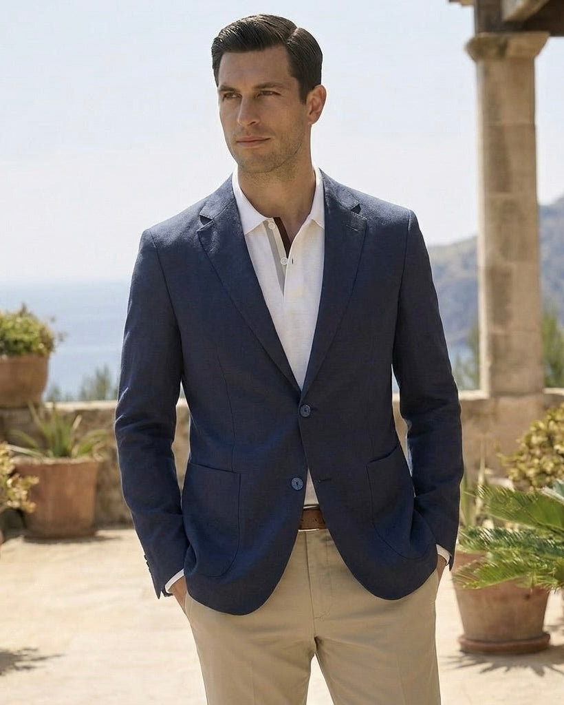 Man in a navy blazer and white shirt standing outdoors with mountains in the background