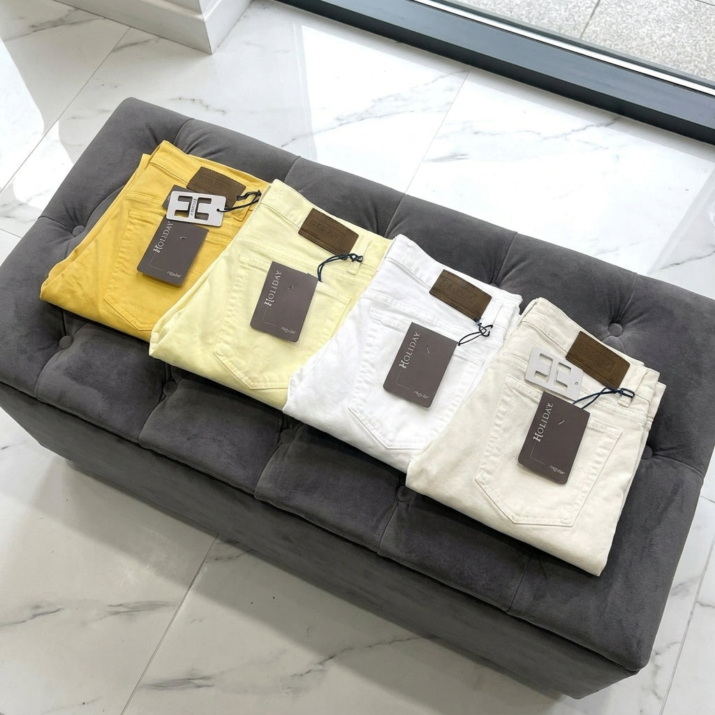 yellow, vanilla, white and off white jeans folded on a gray cushion with tags, on a marble floor.
