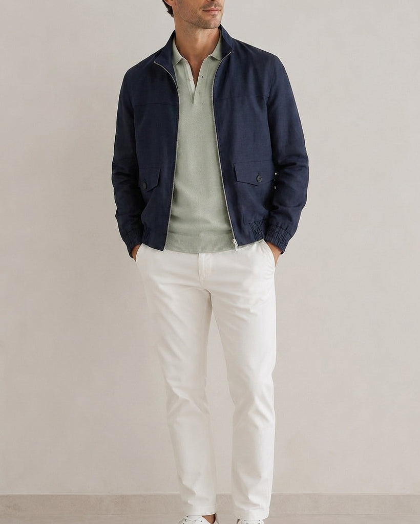 Man wearing a navy jacket, light green shirt, and white pants against a plain background