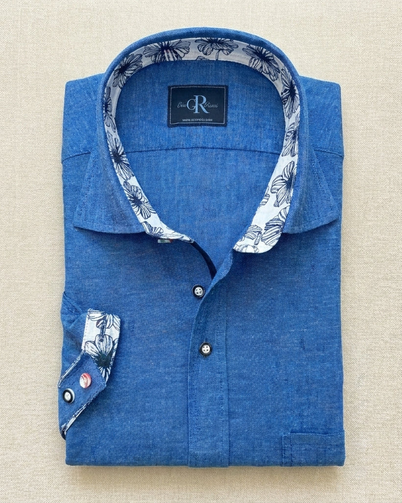 Folded blue shirt with floral collar and cuffs on a beige background