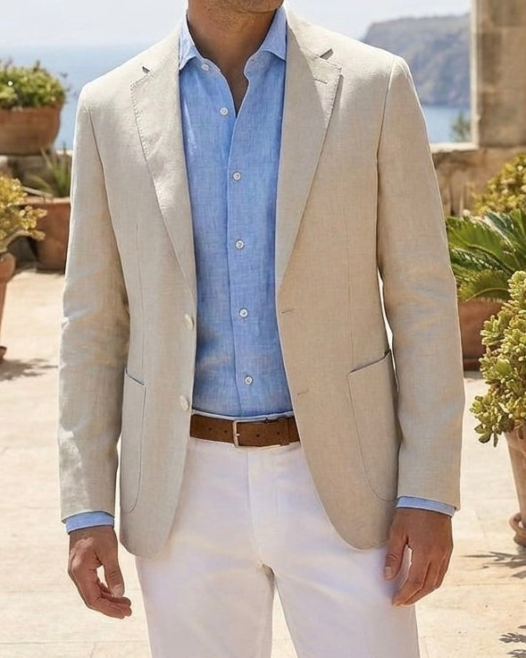 Man in a beige blazer and white pants standing outdoors with plants and columns in the background
